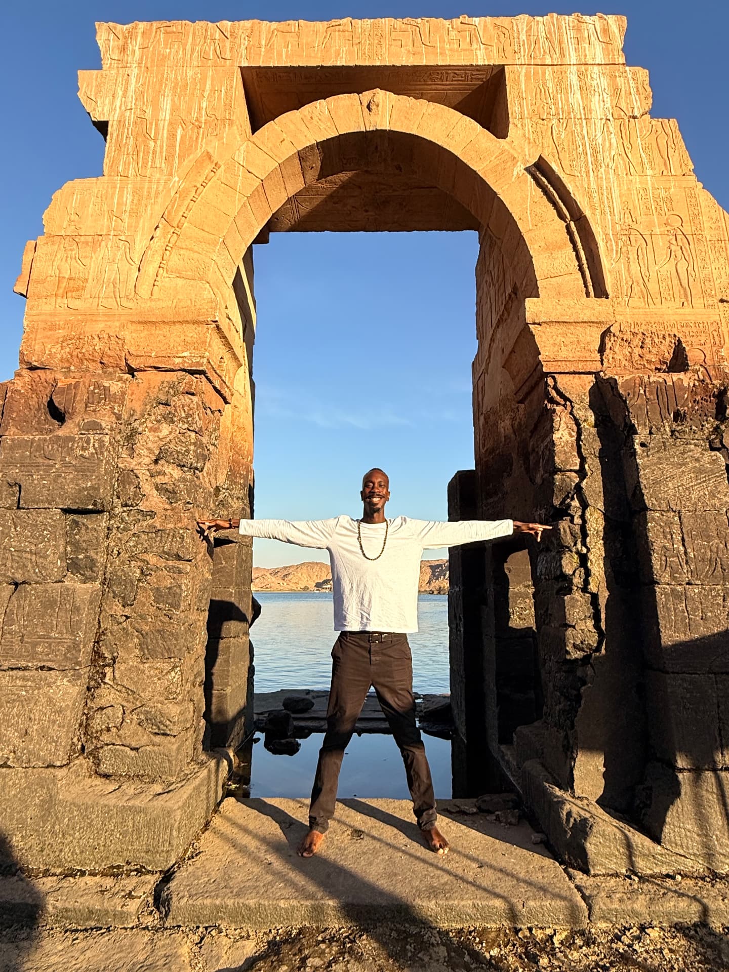 A man with arms outstretched in the ancient gateway at the Temple of Auset/Isis on the Nile, Aswan, Kemet.