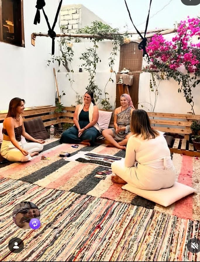 Four women seated in a courtyard circle beneath flowering bougainvillea